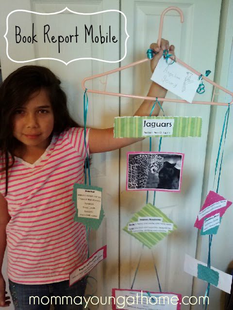 A miss stands future to an book report mobile created from a wire hanger and index cards as in example of creative book report ideas